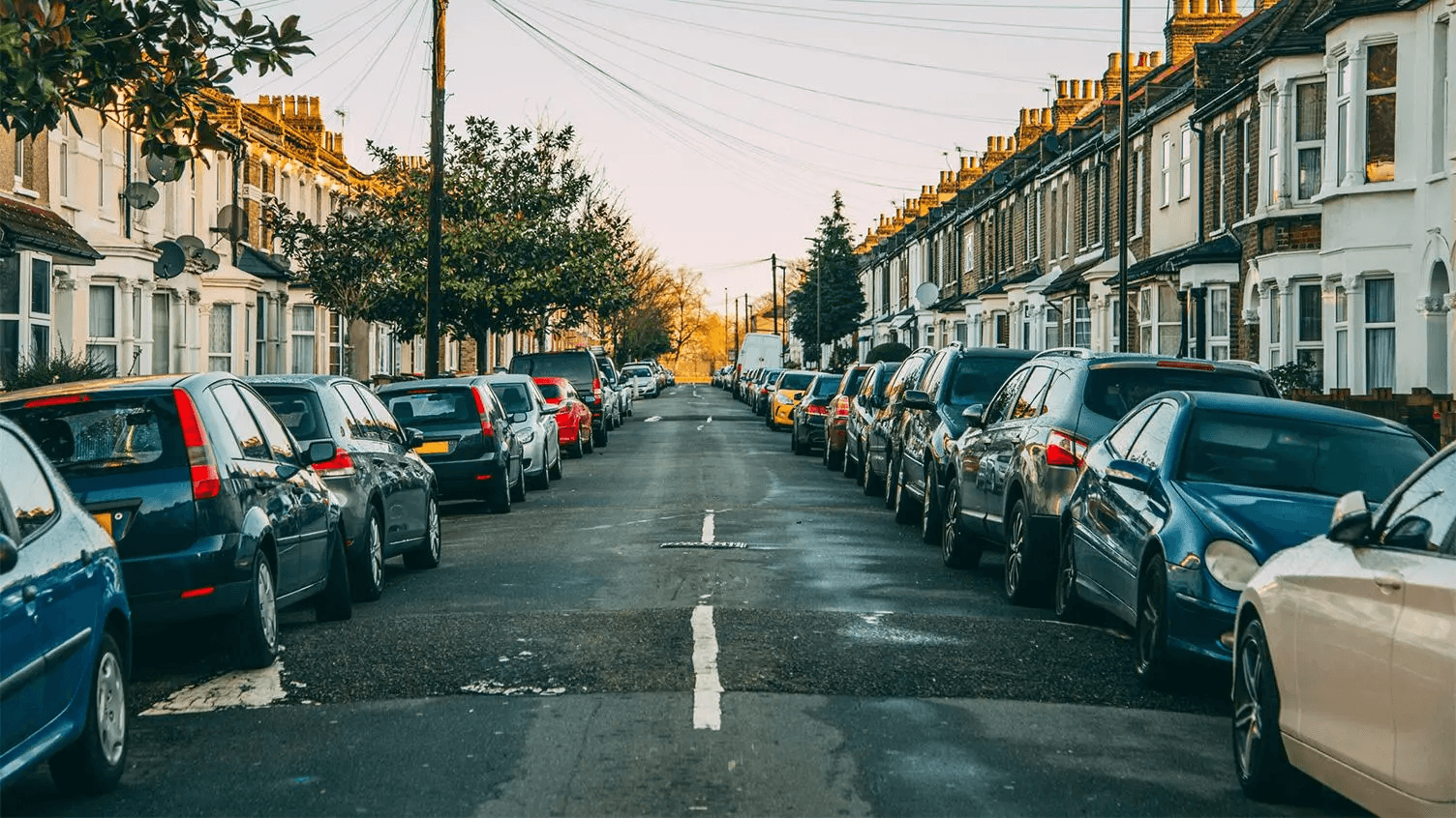 London neighbourhood with 2 storey houses on a long street with cars lining each side of the road.